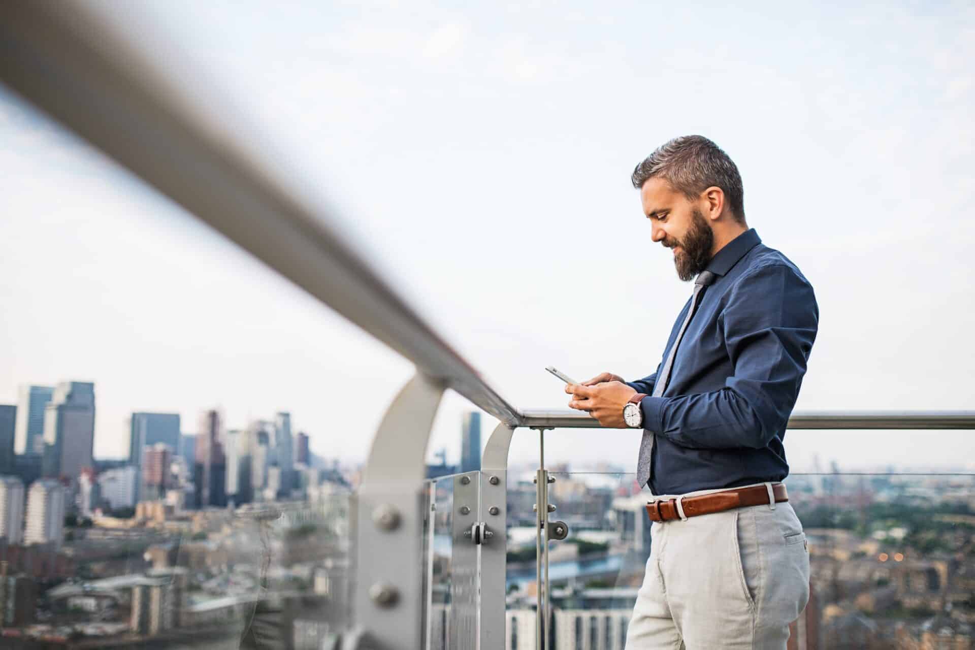 A portrait of businessman with smartphone standing against London view panorama., UK Expansion Worker Visa,