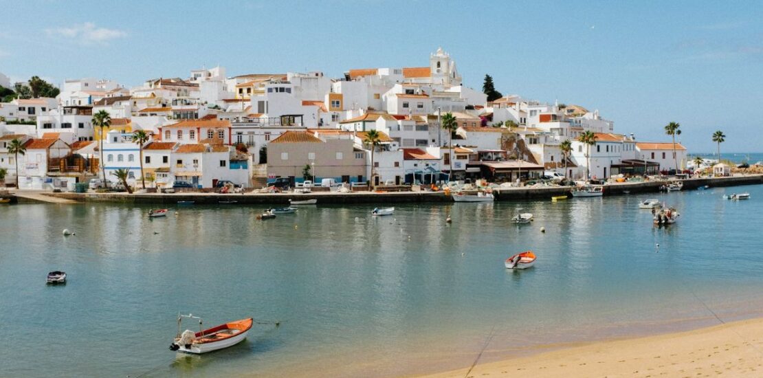 beach with boats in the water and houses on a hill Algarve, Portugal